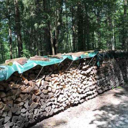 Holzstapel abgedeckt mit grüner Abdeckplane aus LKW Plane.