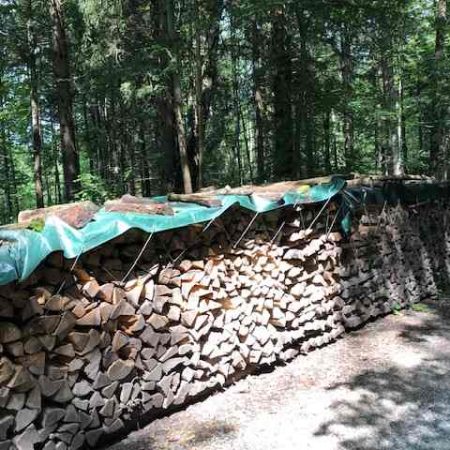 Holzstapel abgedeckt mit grüner Abdeckplane aus LKW Plane.