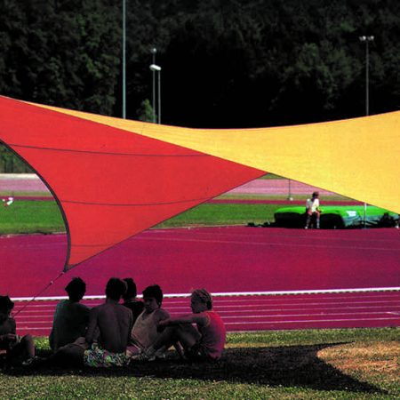Auf einer Wiese, am Sportplatz, sitzende Kinder unter einem Sonnensegel