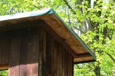 Baumhaus aus Holz im Wald. Dach ist abgedeckt mit grüner Abdeckplane.